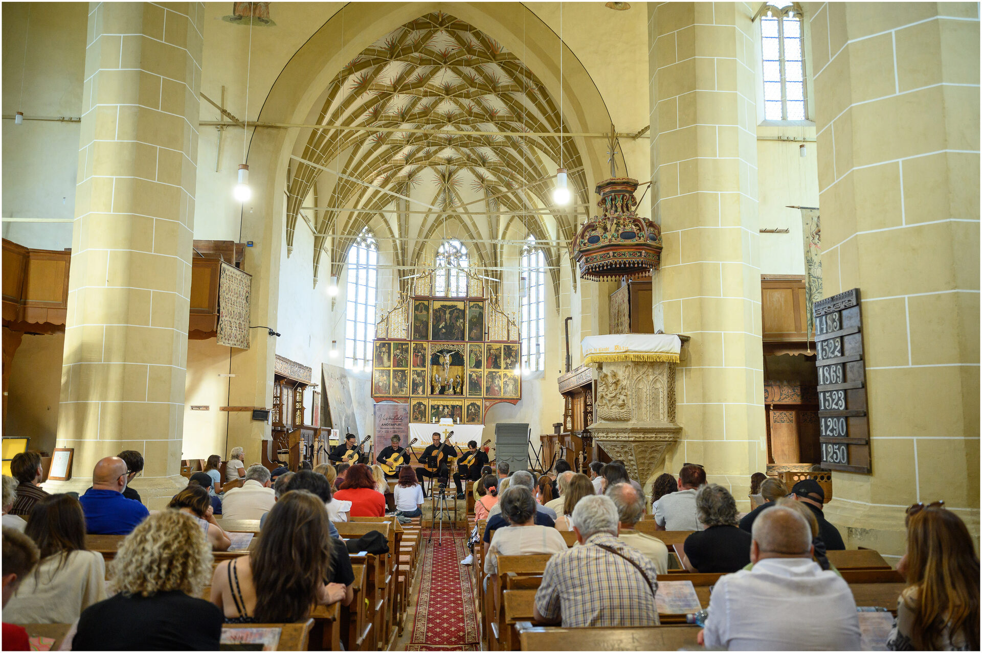 Interior de biserică gotică privit dinspre navă, cu cvartetul cântând lângă altar.