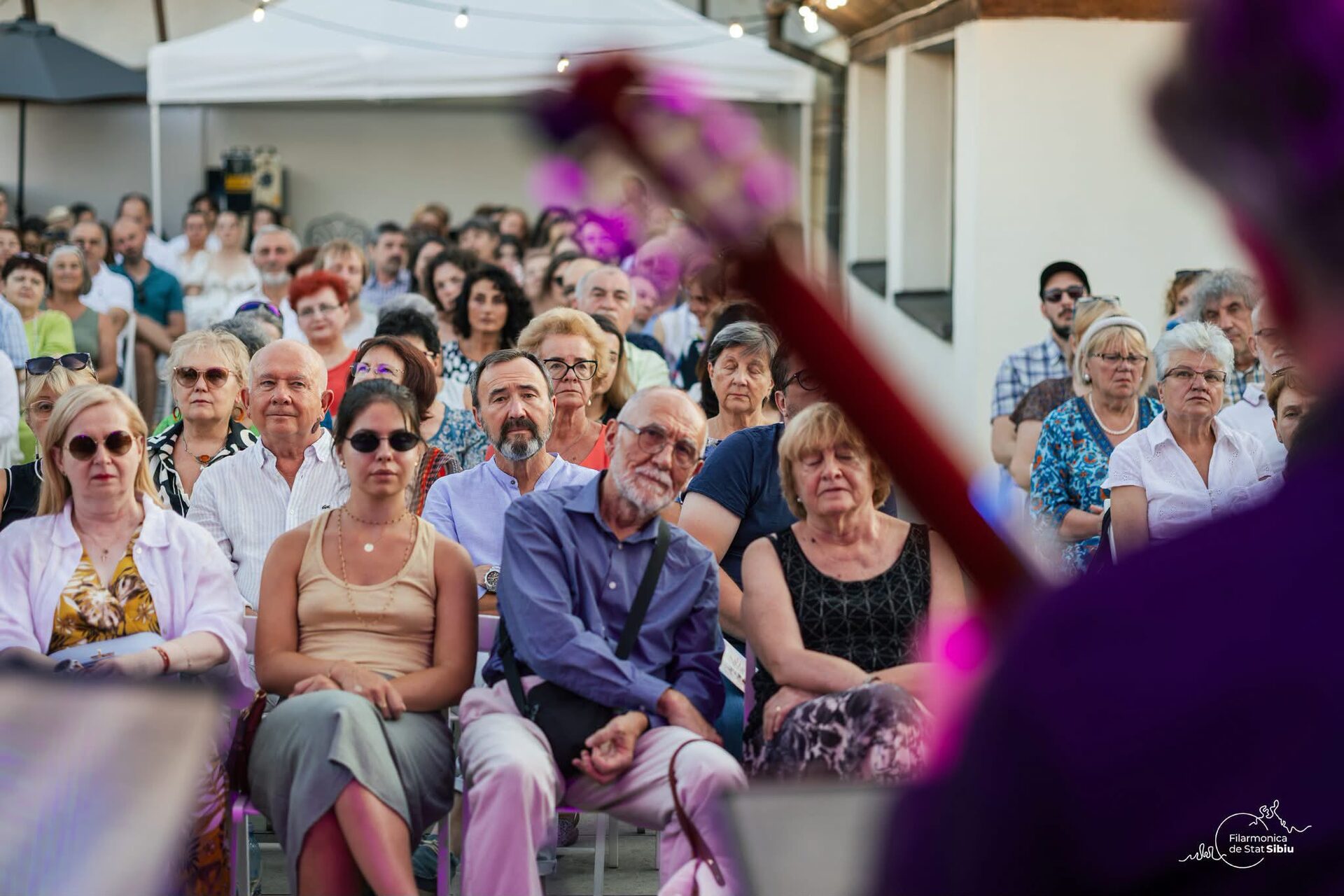 Public numeros la un concert în aer liber, sub un cort, într-o seară de vară.