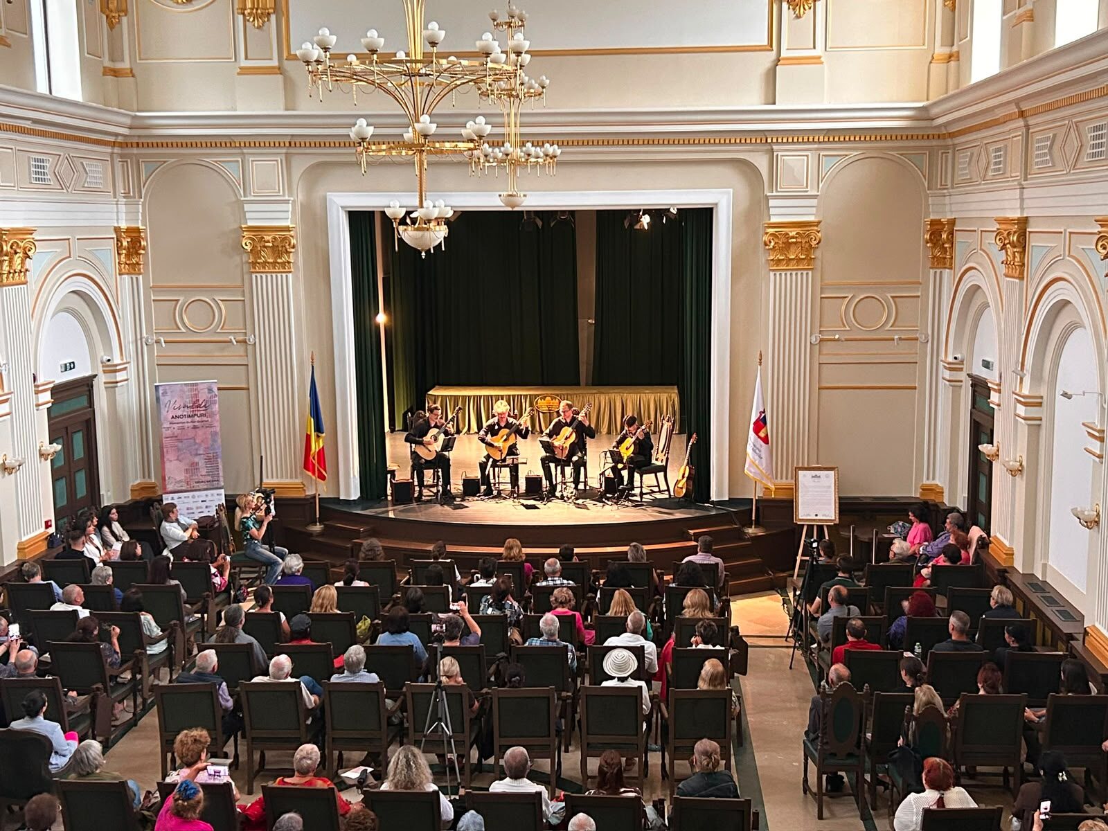 Public numeros într-o sală somptuoasă cu candelabre aurii și coloane.