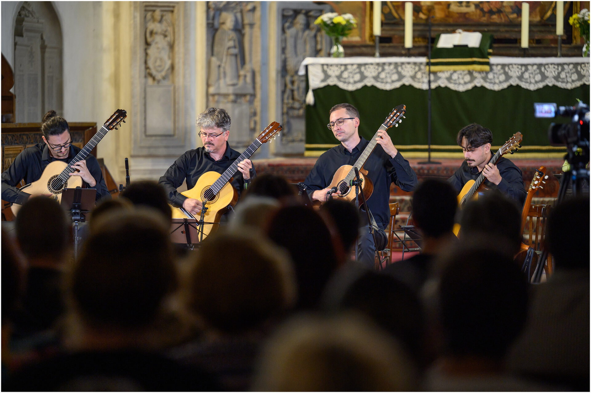 Cei patru chitariști ai Romanian Guitar Quartet cântând în fața altarului unei biserici.